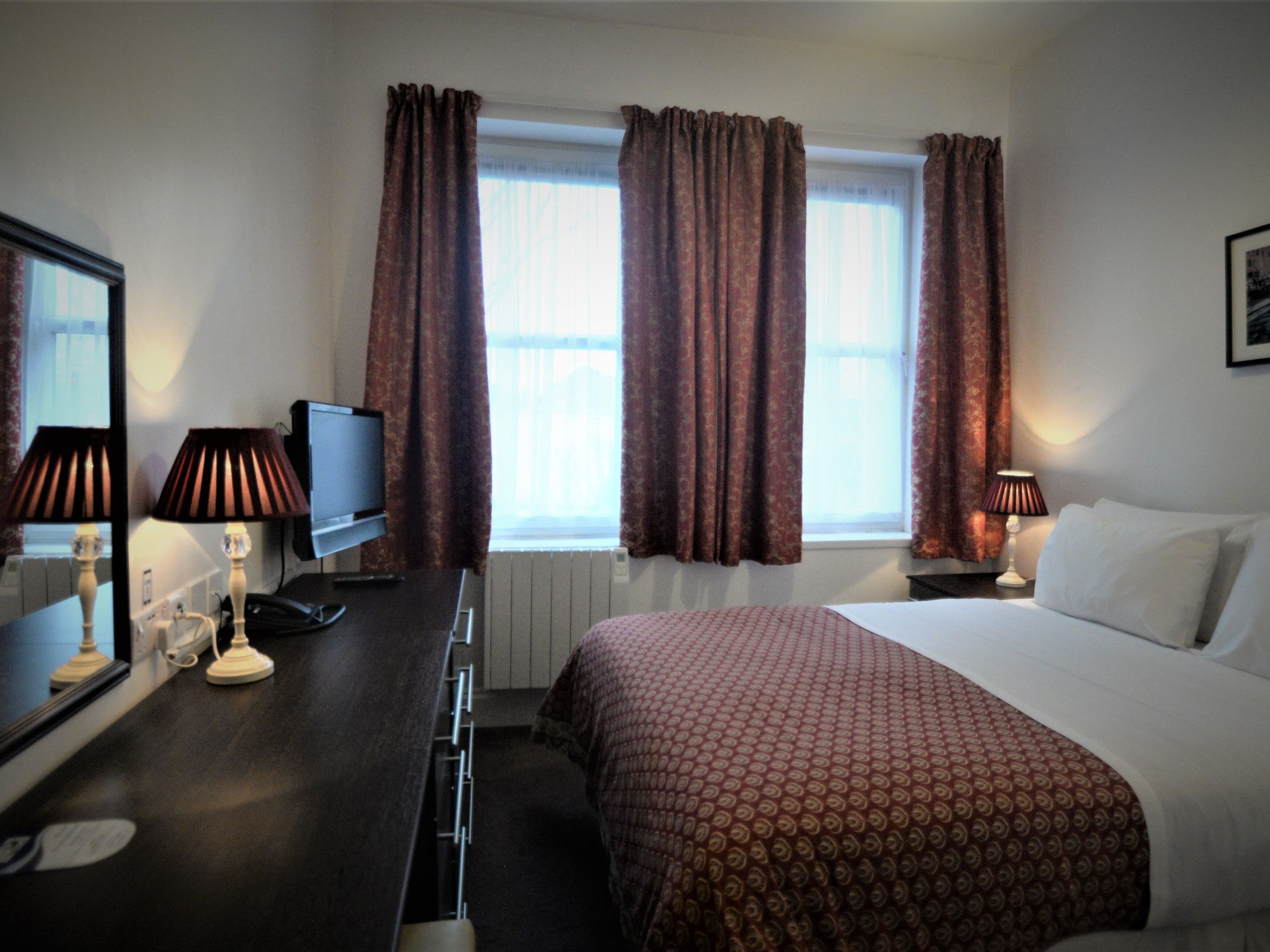 A hotel room with a bed, a desk with a computer, a TV, and two lamps.