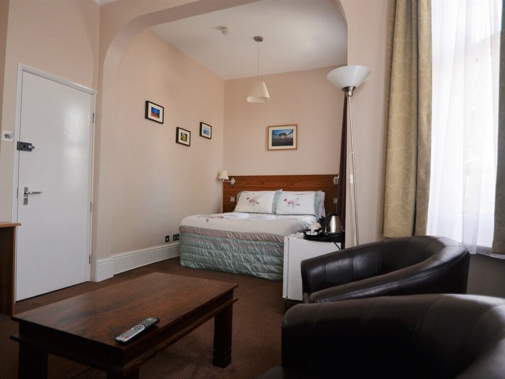 A hotel room with a bed, a desk, a chair, and a lamp.