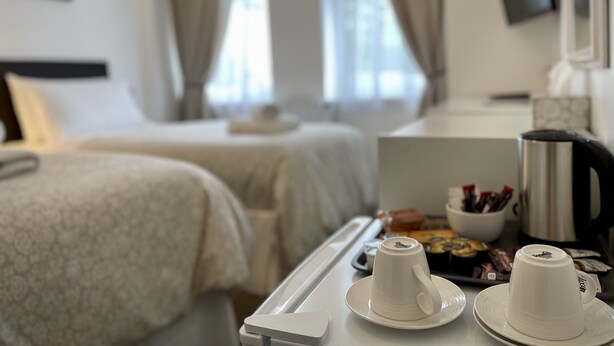 A hotel room with a bed, a bedside table with a tray of pastries, and a coffee maker. - Gateway Hotel (London)