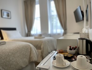 Quarto de hotel com cama, mesa de cabeceira com bandeja de doces e cafeteira.