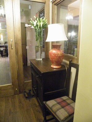 A wooden cabinet with a lamp and a vase of flowers. - Saracens Head Towcester by Greene King Inns (Towcester)