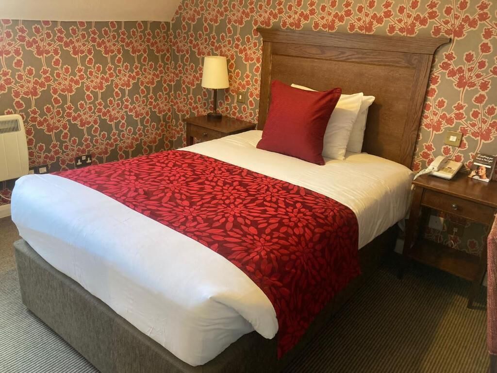 A hotel room with a large bed, a wooden headboard, a nightstand with a lamp, and a telephone.