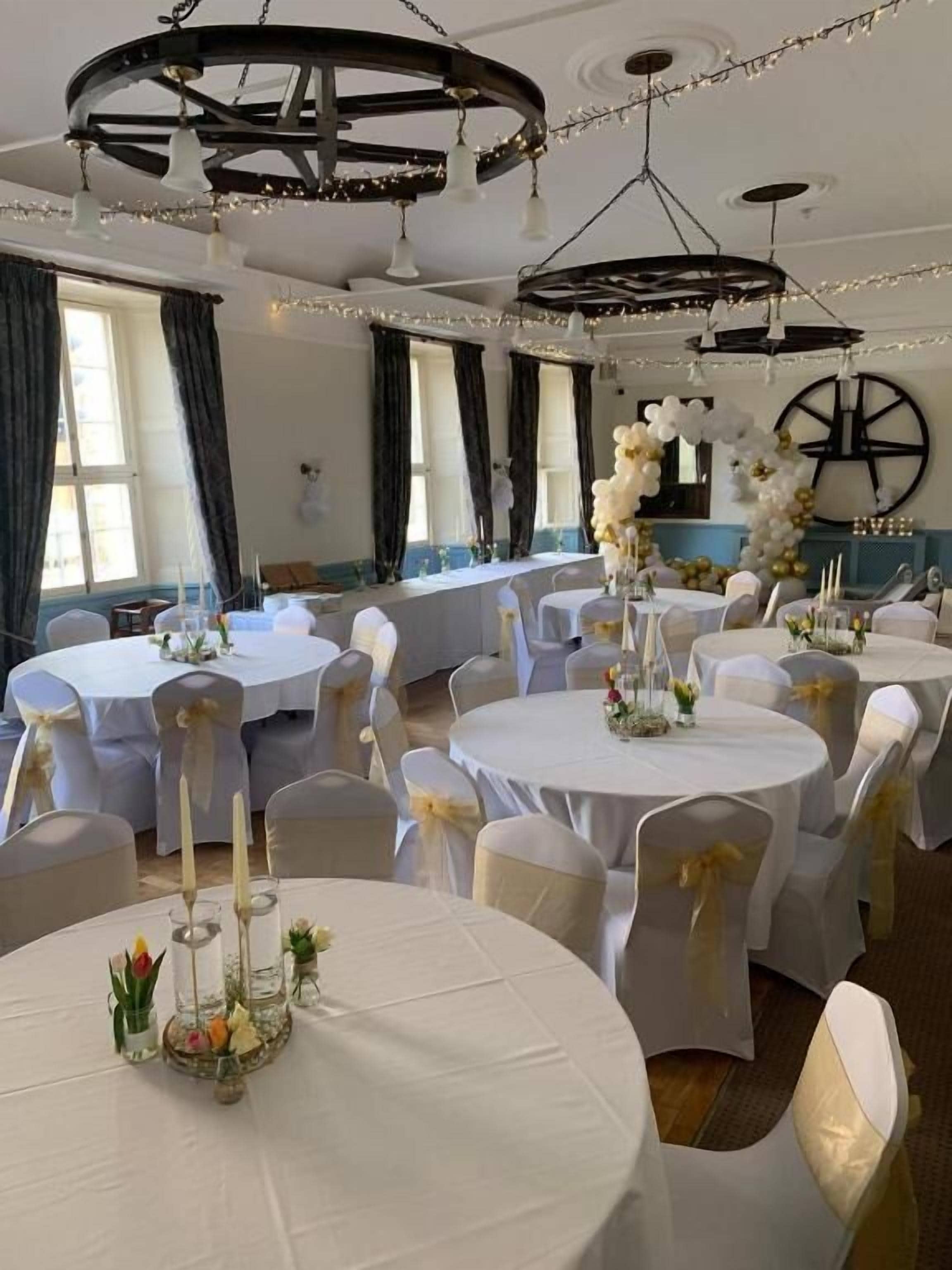 A banquet hall with round tables, white tablecloths, and chairs with gold sashes.