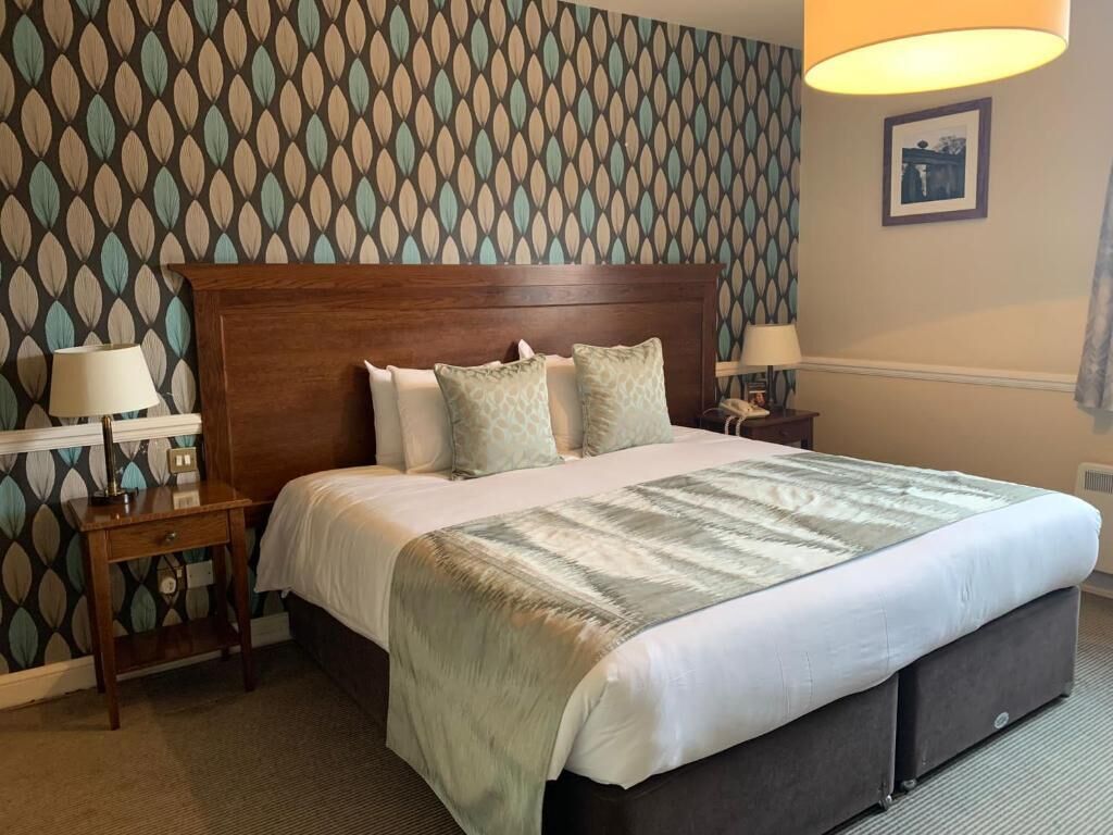 Ein Hotelzimmer mit einem großen Bett, zwei Nachttischen, einer Wand mit gemustertem Tapeten und einem einzelnen gerahmten Bild.
