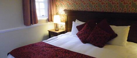 Habitación de hotel con una cama bien hecha, una mesita de noche con lámpara y una ventana con cortinas.