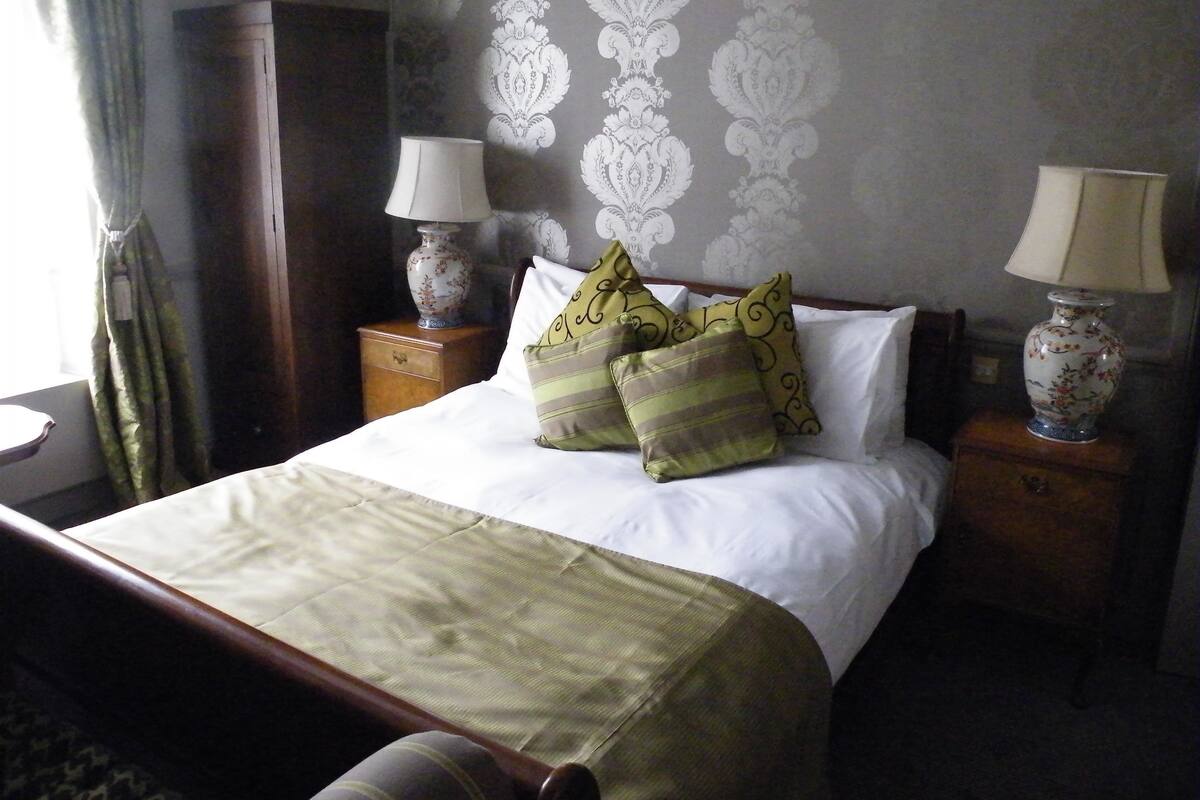 Una cama bien hecha con almohadas, una mesita de noche con lámpara y un aparador.