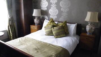 A neatly made bed with pillows, a nightstand with a lamp, and a dresser.