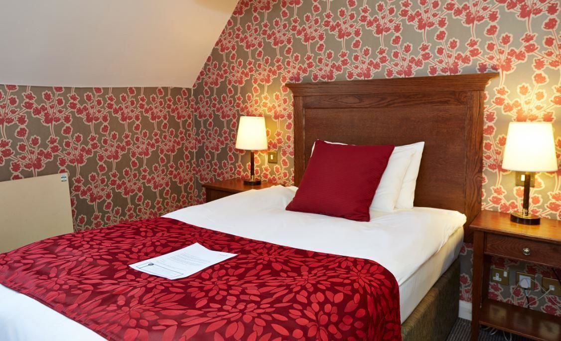 Een hotelkamer met een bed, twee bedlampen, bloemenbehang en een rode sprei.
