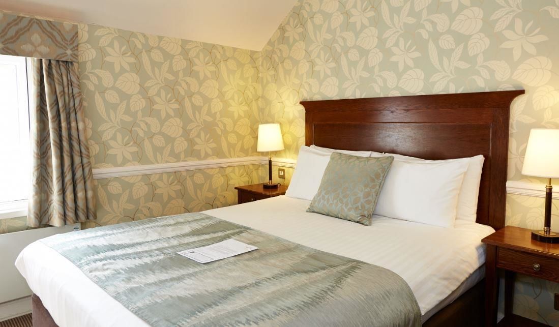 A hotel room with a large bed, two bedside tables, a window with curtains, and floral wallpaper.
