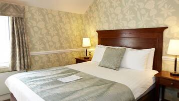 A hotel room with a large bed, two bedside tables, a window with curtains, and floral wallpaper.
