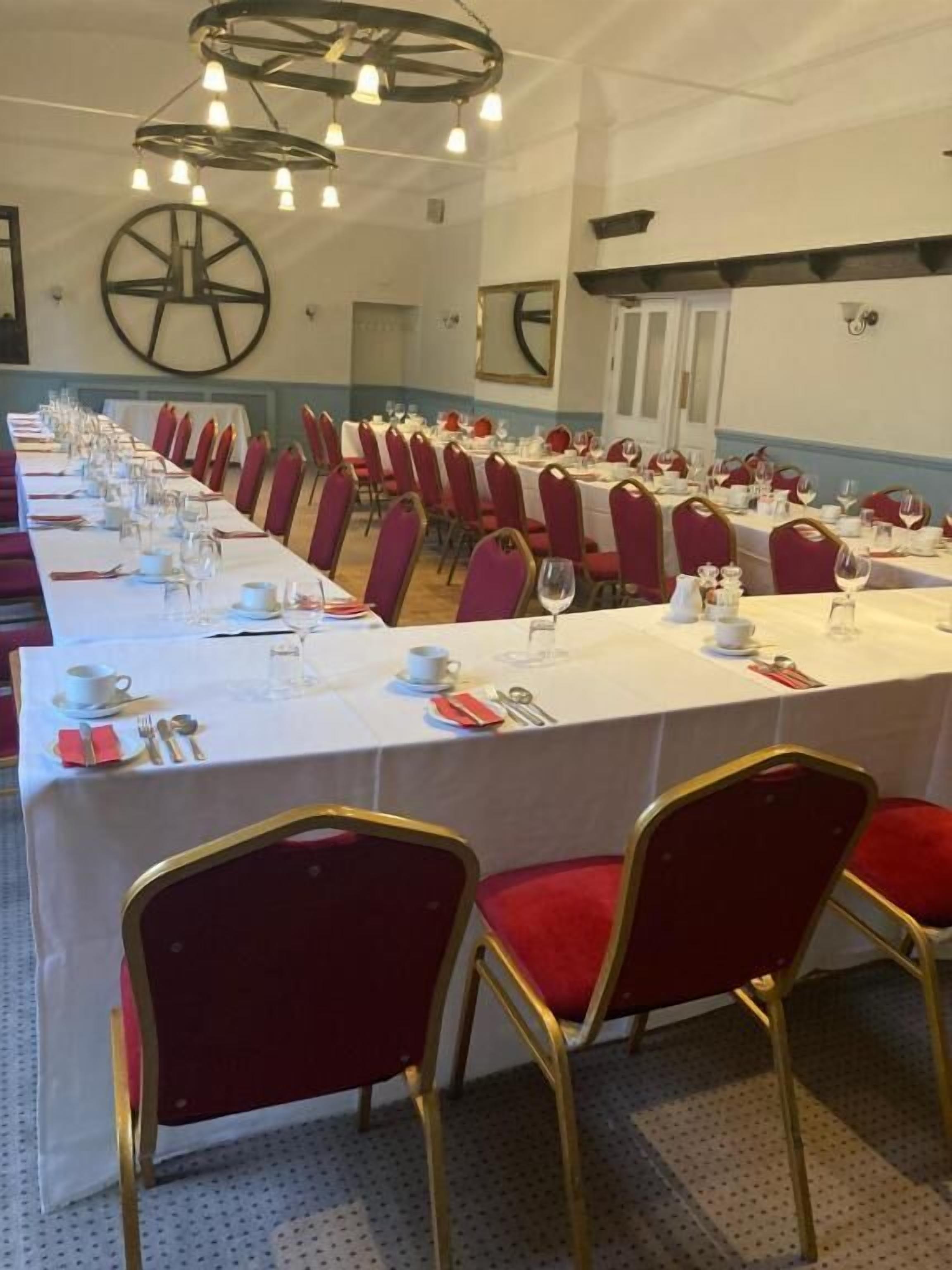A conference room with long tables set for a meeting, red chairs, and a large wheel decoration on the wall.