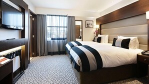 A hotel room with a large bed, a TV mounted on the wall, a desk with a lamp, and a window with curtains. - Paddington Court Rooms (London)