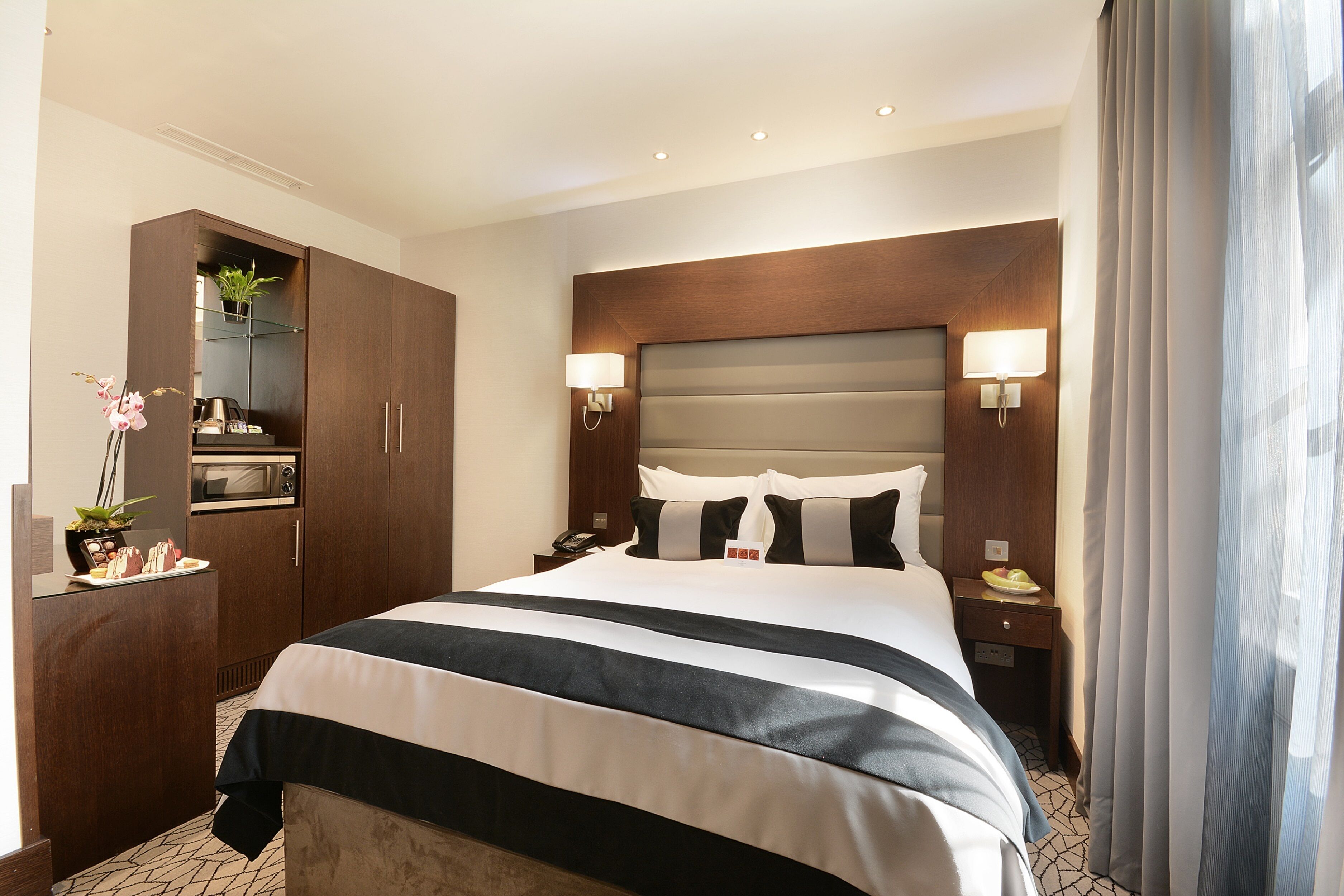 Une chambre d’hôtel avec un grand lit, un minibar, un bureau avec une lampe et une vue sur l’extérieur.