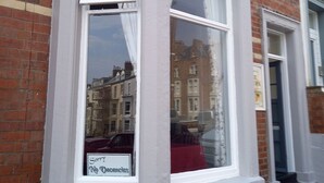 A corner bay window with white trim, brick wall, and a reflection of buildings in the glass. - The Europa (Whitby)
