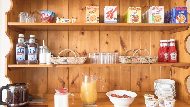 A breakfast bar with shelves stocked with cereals, condiments, and beverages. - The Europa (Whitby)