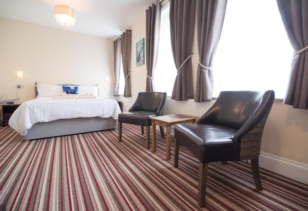 Habitació d'hotel amb un llit, dues cadires, una taula petita i un terra amb moqueta.