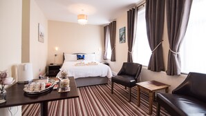 A hotel room with a bed, a desk with a tray of breakfast items, a chair, a small table, and a window with curtains. - The Europa (Whitby)
