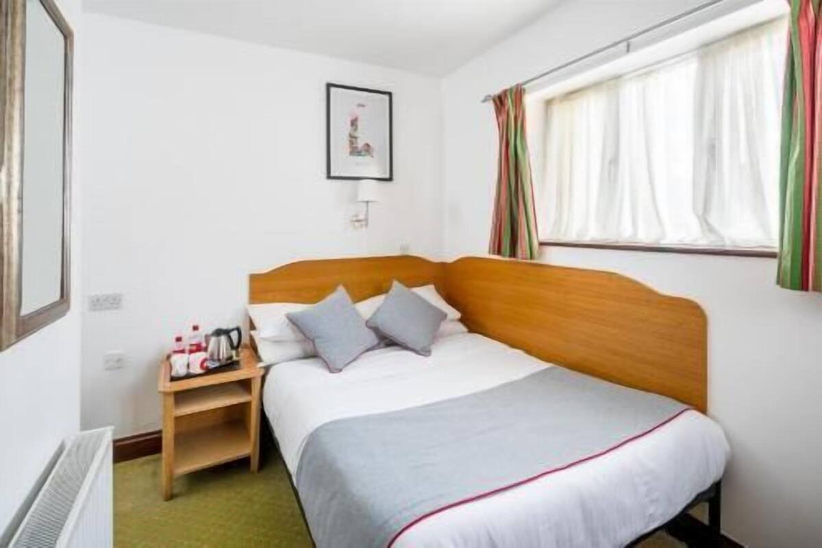 A hotel room with a single bed, a bedside table with a lamp, a framed picture on the wall, and a window with curtains.