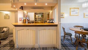 A bar area with a counter, shelves of bottles, and a dining table with chairs. - Castletown Hotel (Thurso)