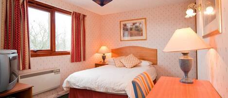 A hotel room with a bed, bedside lamp, TV, and a window with curtains.