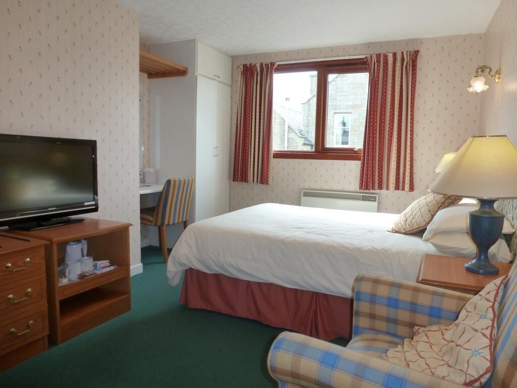 Una habitación de hotel con cama, televisión, escritorio con lámpara y una silla.