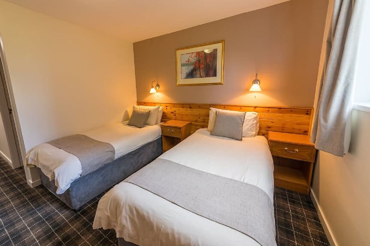 A hotel room with two beds, a painting on the wall, and two bedside lamps.