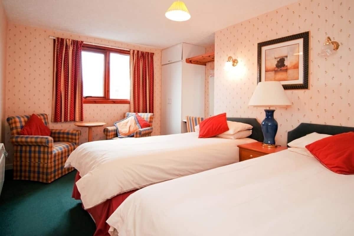 A hotel room with two beds, a chair, a table, a lamp, and a picture on the wall.