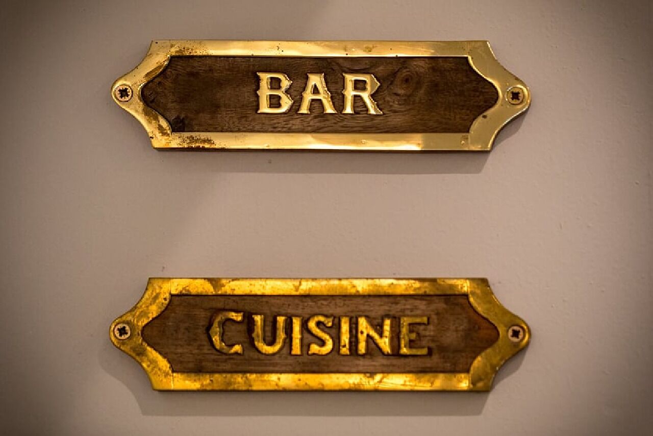 Dos letreros de madera con bordes metálicos, uno con la palabra 'BAR' y el otro con la palabra 'CUISINE'.