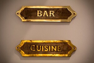 Dos letreros de madera con bordes metálicos, uno con la palabra 'BAR' y el otro con la palabra 'CUISINE'.