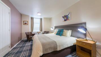 Een hotelkamer met een bed, nachtkastje, lamp, stoel en een raam met gordijnen.