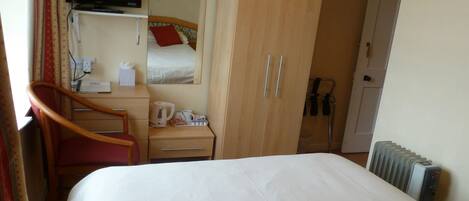 Una habitación de hotel con cama, escritorio y silla, armario, televisor montado en la pared y radiador.