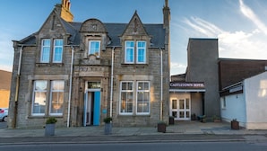 A historic stone building with a traditional architectural style, featuring a prominent entrance with a blue door, multiple windows, and a sign for Castleletown Hotel. - Castletown Hotel (Thurso)