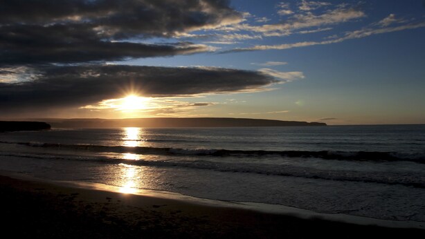 A beach with the sun setting over the ocean, creating a silhouette of clouds against the sky. - Castletown Hotel (Thurso)