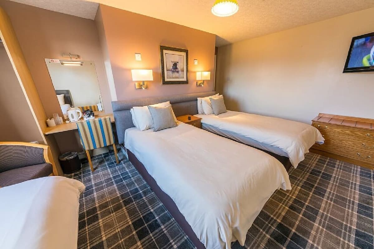 A hotel room with two beds, a desk with a chair, a mirror, and a television.