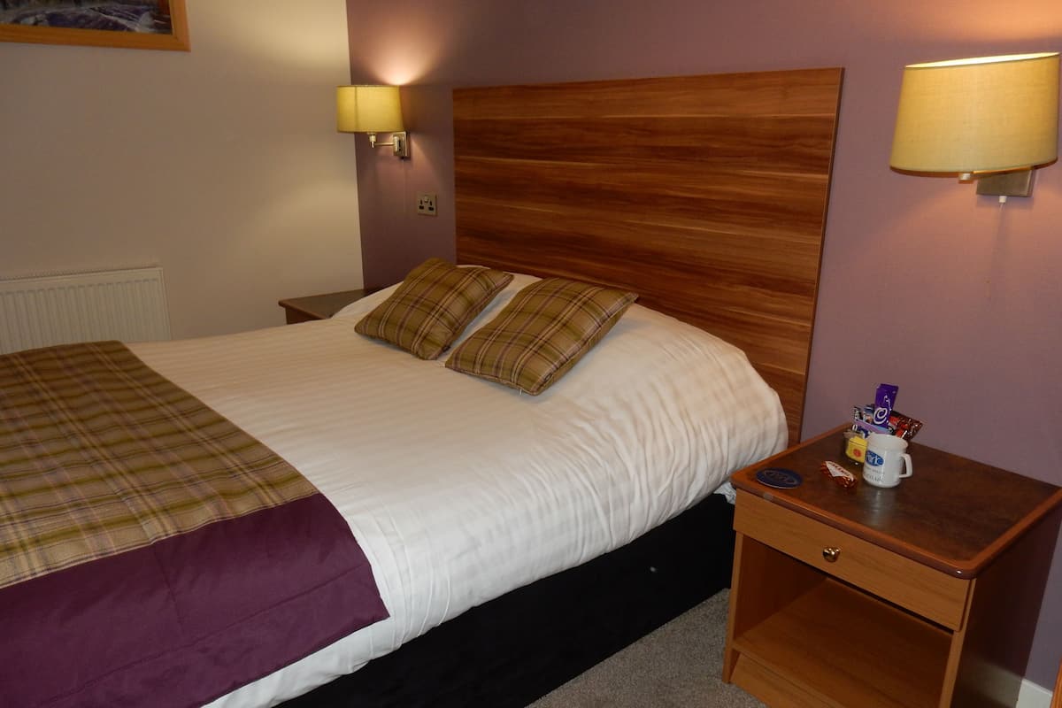 A neatly made bed with a plaid blanket, two pillows, and a wooden headboard. There are two wall-mounted lamps on either side of the bed.
