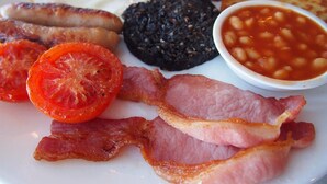 Ein Teller mit Speck, Eiern, Würstchen, Pilzen, Blutwurst, Tomaten und gebackenen Bohnen.