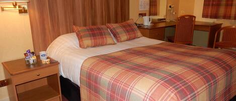 Quarto de hotel com uma cama grande, duas almofadas, mesa de cabeceira com abajur, escrivaninha com cadeira e espelho.