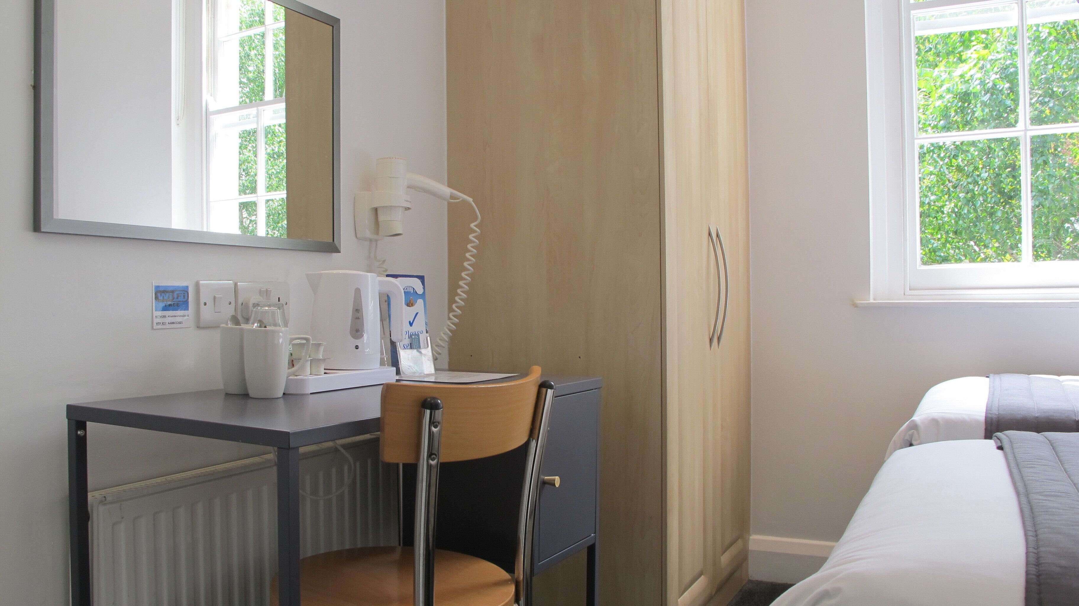 Hotellihuone, jossa on sänky, työpöytä tuolilla, kahvinkeitin, puhelin ja ikkuna, josta on näkymä vehreään maisemaan.
