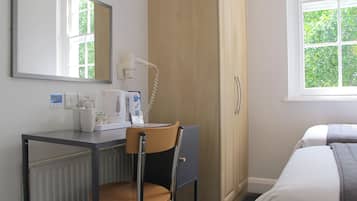 Habitación de hotel con cama, escritorio con silla, cafetera, teléfono y ventana con vista a vegetación.