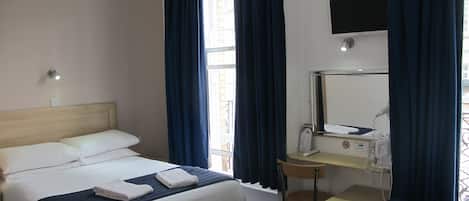 A hotel room with a bed, a desk, a chair, a mirror, and a window with curtains.