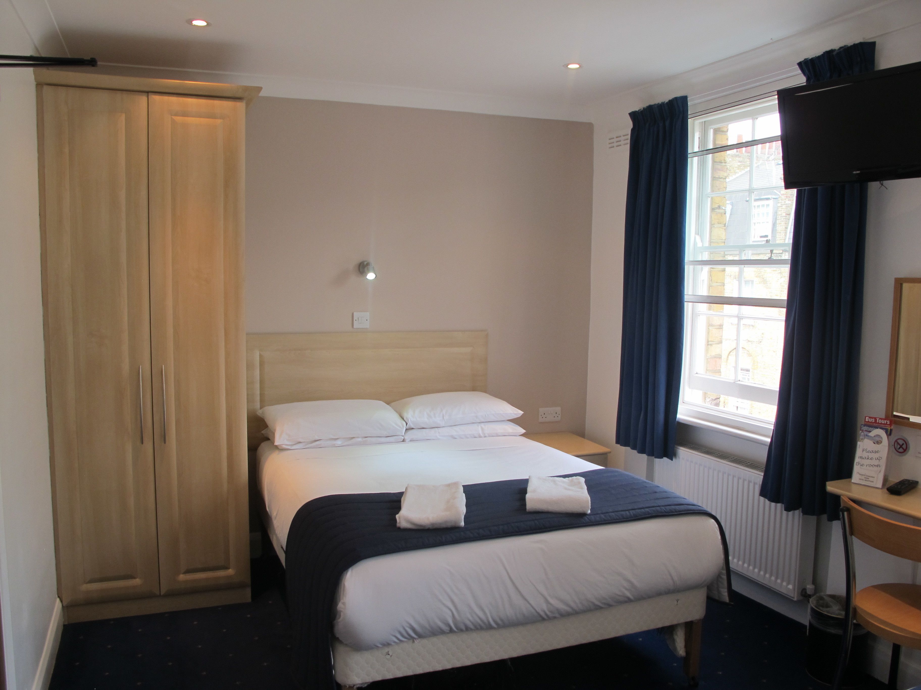 Een hotelkamer met een bed, een kledingkast, een nachtkastje, een raam met gordijnen en een televisie aan de muur.