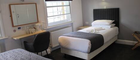 Een hotelkamer met een bed, nachtkastje, stoel en een raam met jaloezieën.