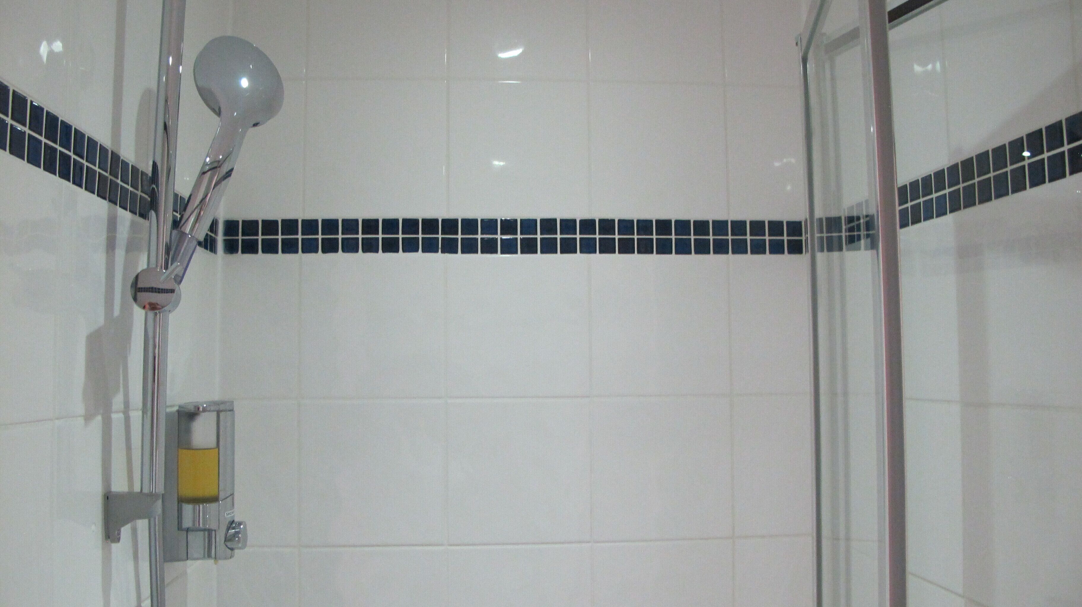 A shower area with a glass door, white tiles, and a blue-tiled accent strip.