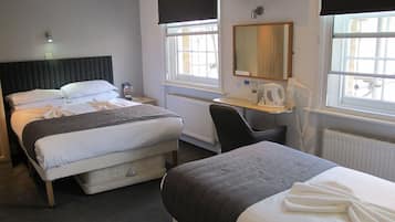A hotel room with a bed, a desk, a chair, a radiator, and a window with a view of the outside.
