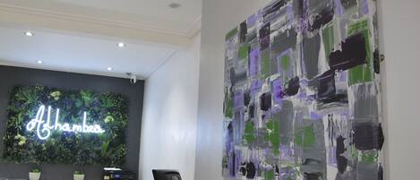 A modern office space with a neon sign reading "Afghanistan" on a dark wall, a large abstract painting, and a reception desk with a printer.