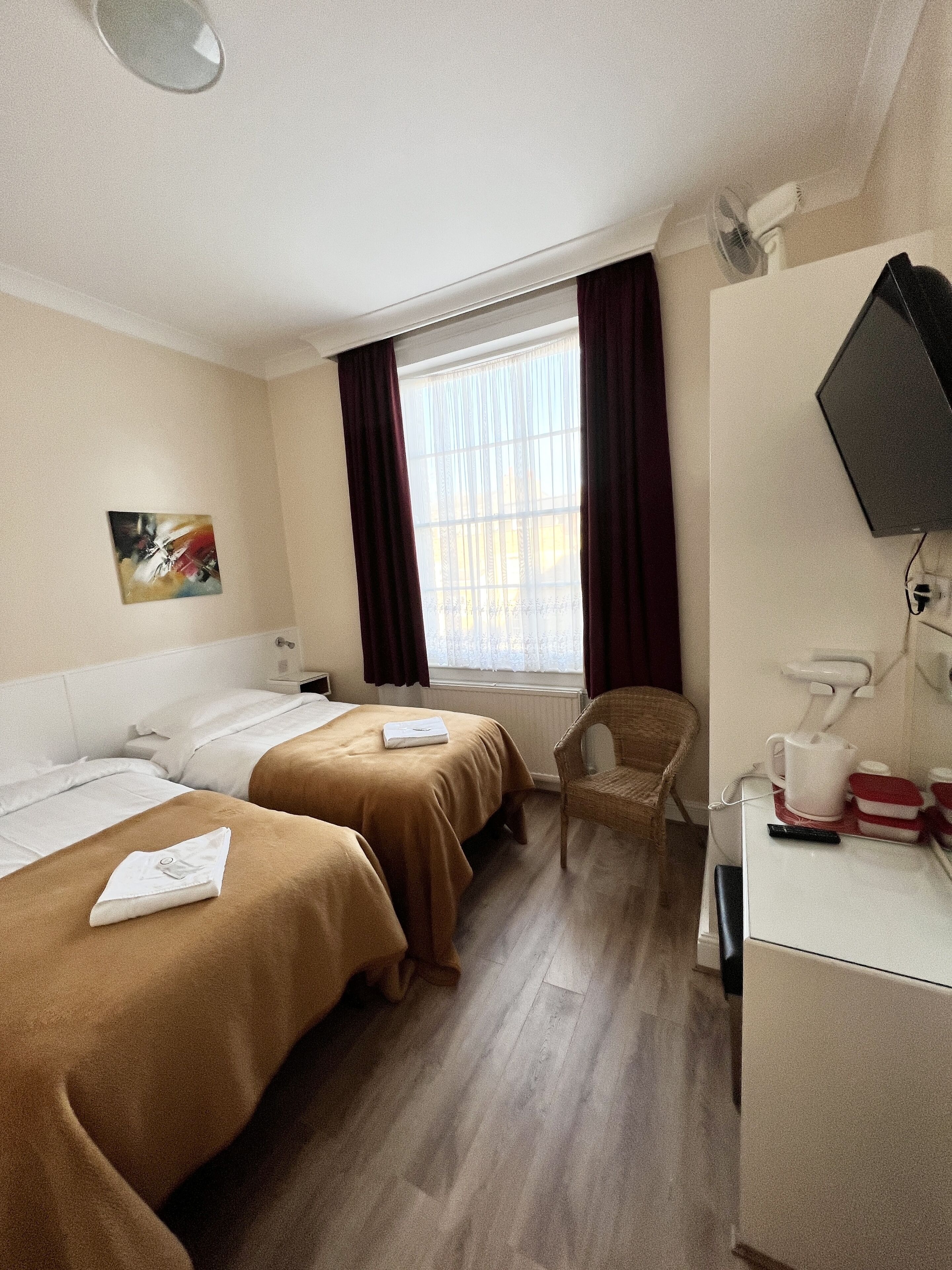 A hotel room with two beds, a chair, a desk with a coffee maker, a TV, and a window with curtains.