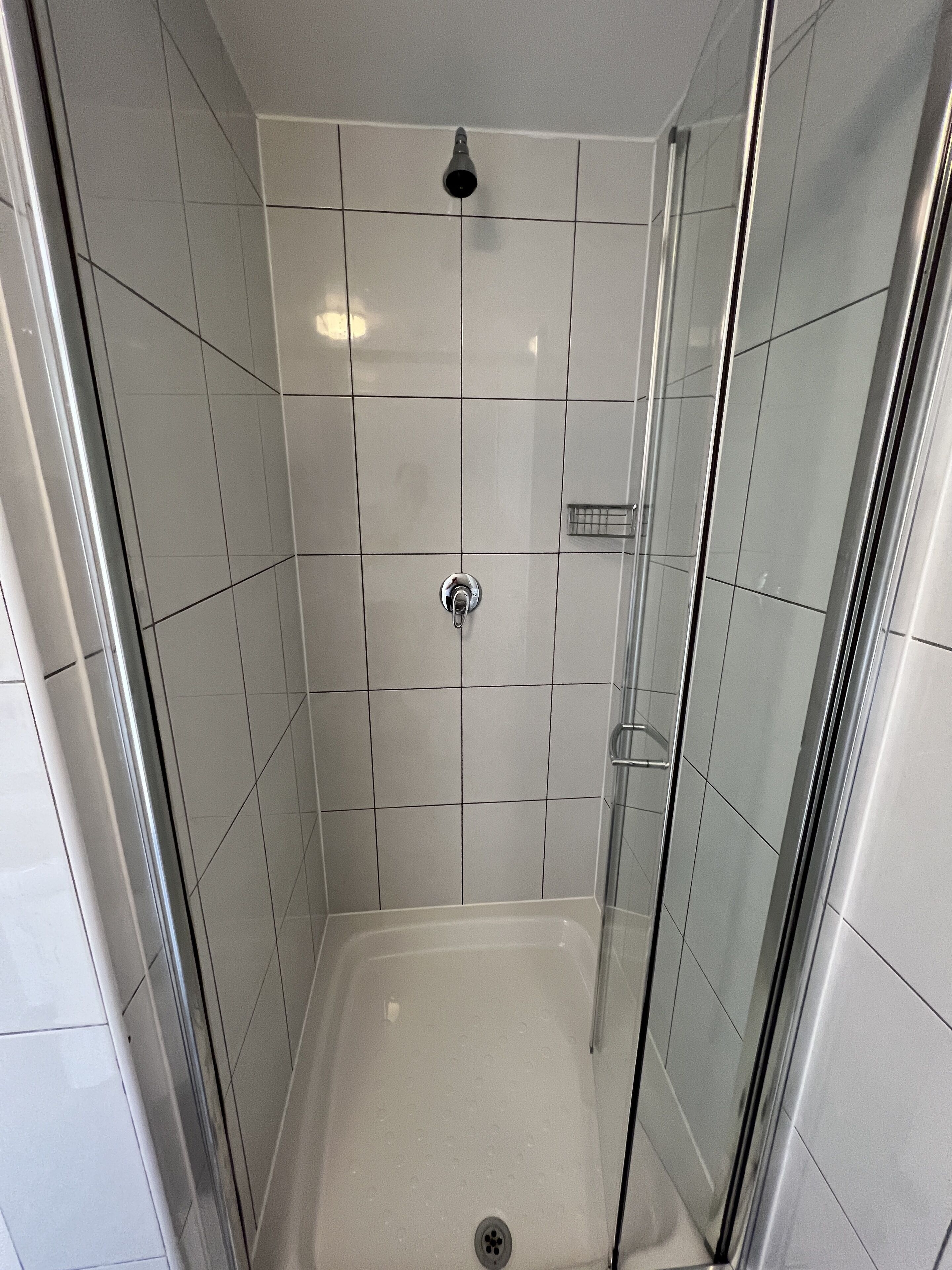 A small, enclosed shower stall with white tiles and a glass door.