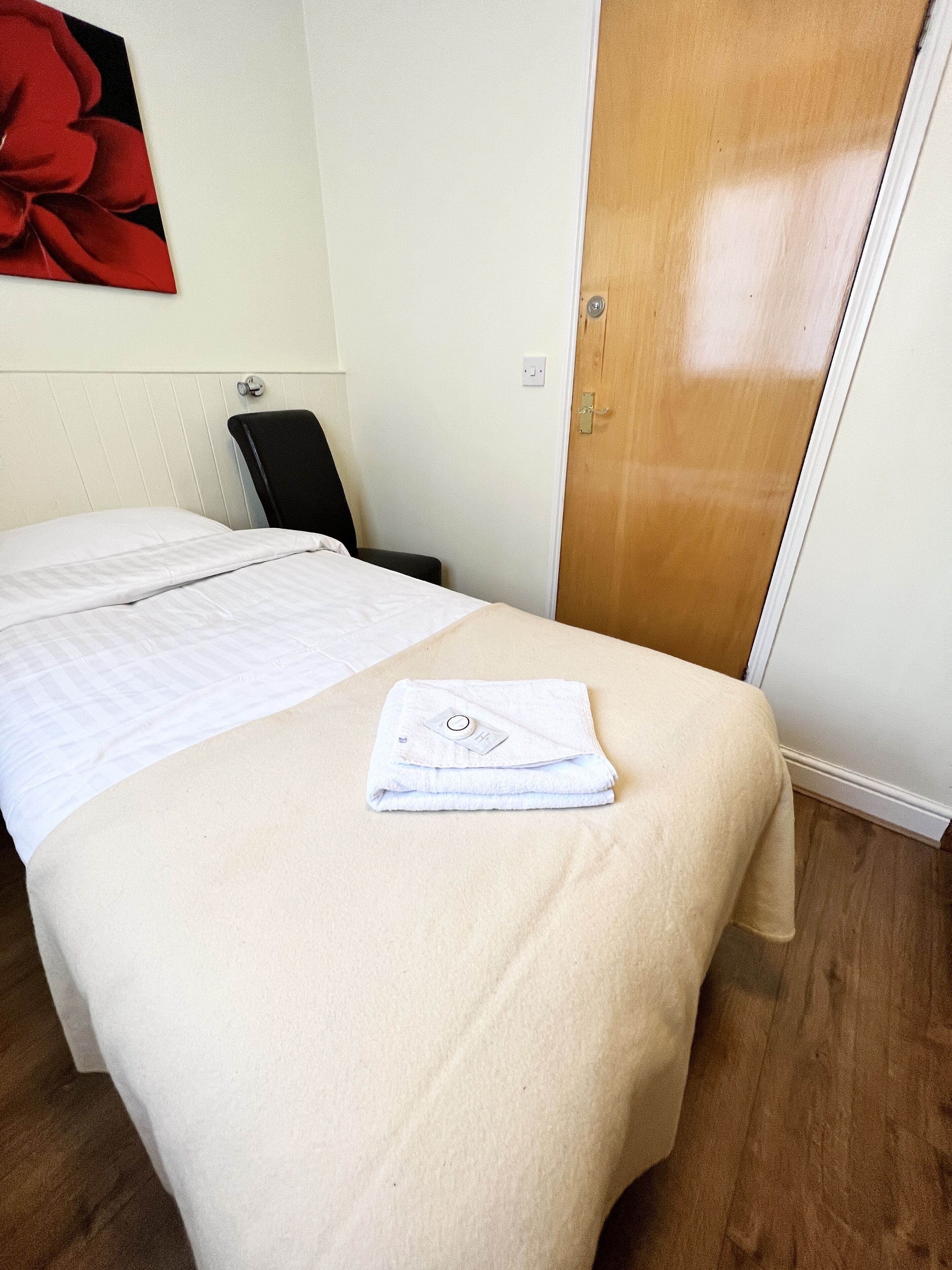 Una habitación de hotel con una cama, una silla, una puerta de madera y un cuadro de una flor roja en la pared.