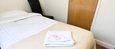 Una habitación de hotel con una cama, una silla, una puerta de madera y un cuadro de una flor roja en la pared.