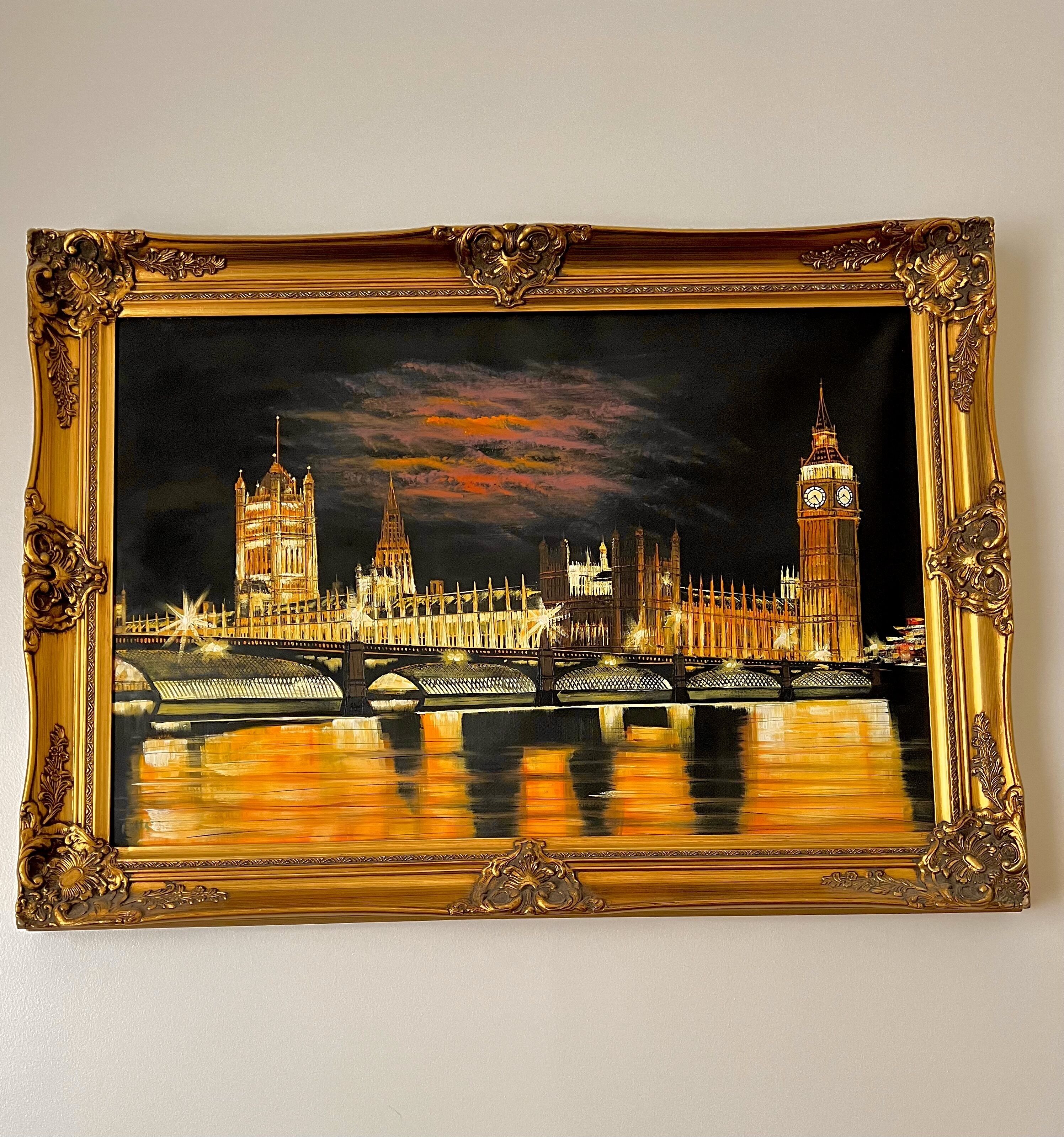 Un tableau encadré représentant une vue nocturne d’une ville, avec ses bâtiments emblématiques et un pont.